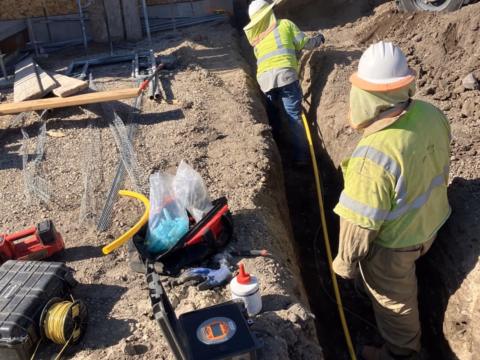 Crew installing yellow gas distribution pipe in an open trench, with pressure test equipment set up at the surface
